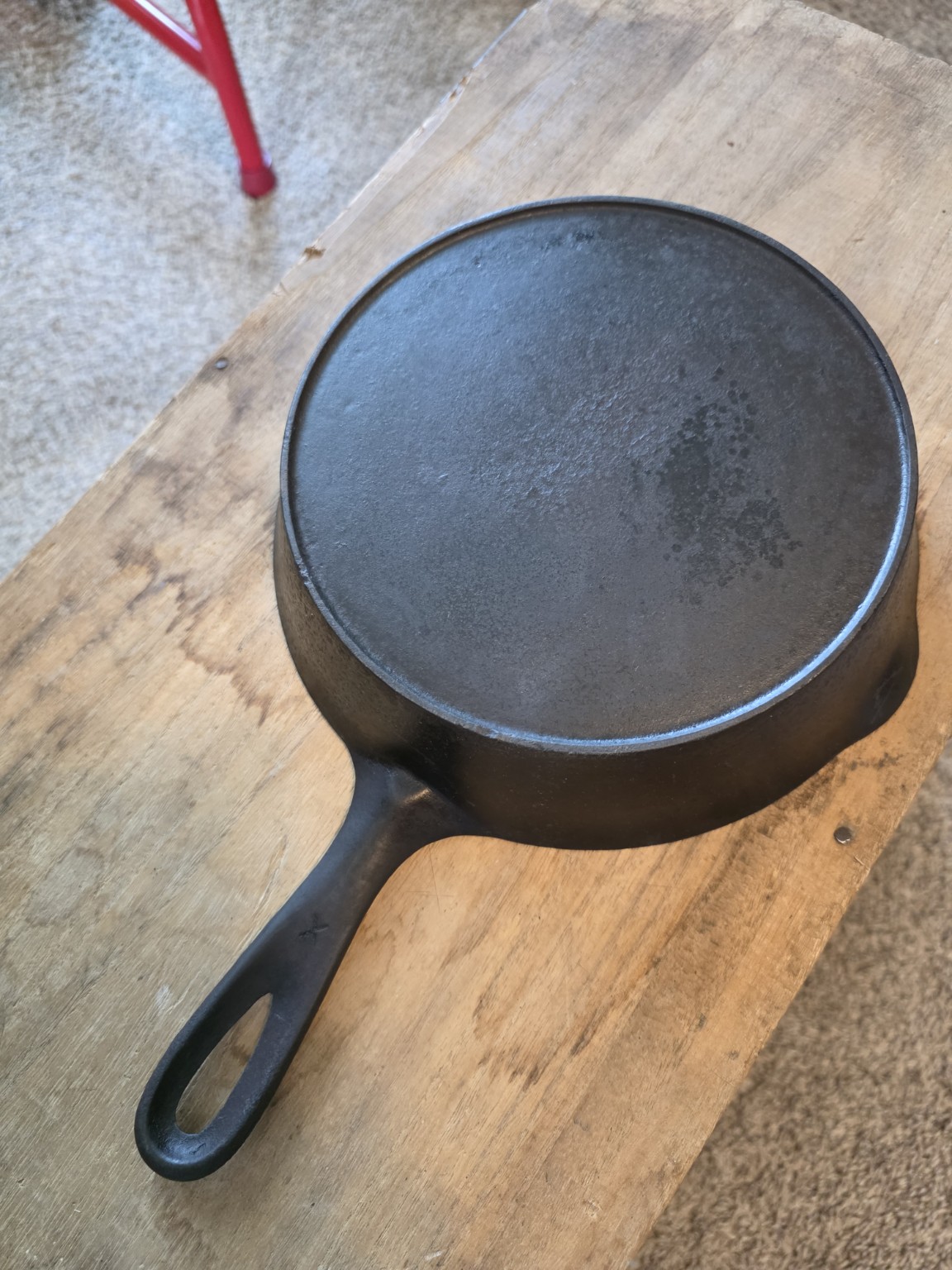 Dark cooking surface of a vintage cast-iron skillet on a wooden bench